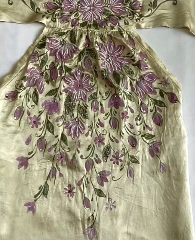 Third development stage showing the finished garment with purple trailing floral embroidery and hotfix rhinestone accents on a pale gold satin base with an olive green cast